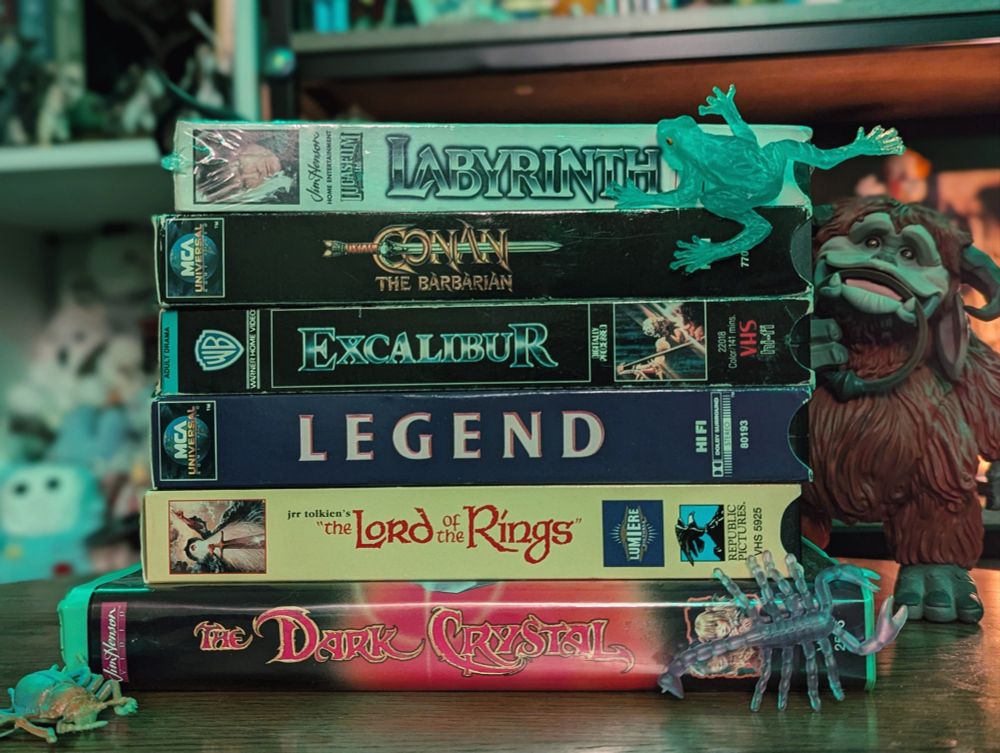 a stack of VHS tapes. plastic bugs and frog. a statue of the character Ludo from the movie Labyrinth is in the background 