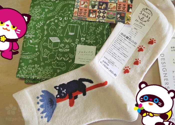 購入した商品の写真です。緑地の背景に白い線で猫や草花のイラストが描かれたハンカチ、黒猫が花を抱きしめているイラストが入ったソックス。