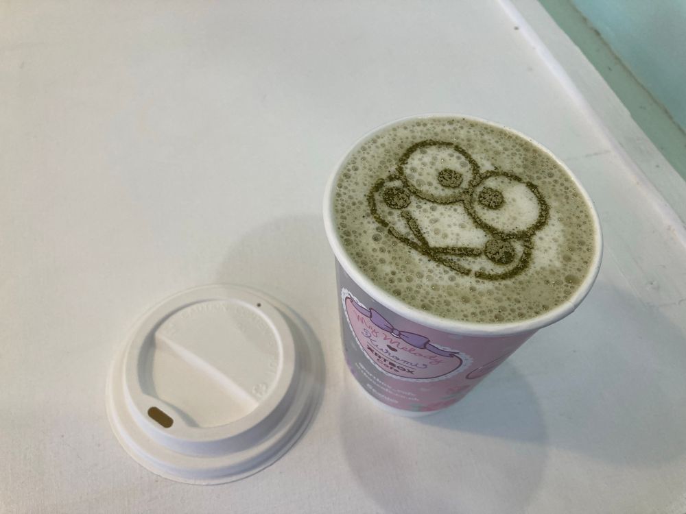 A keroppi matcha latte. A kawaii frog face sits on top of the drink.
