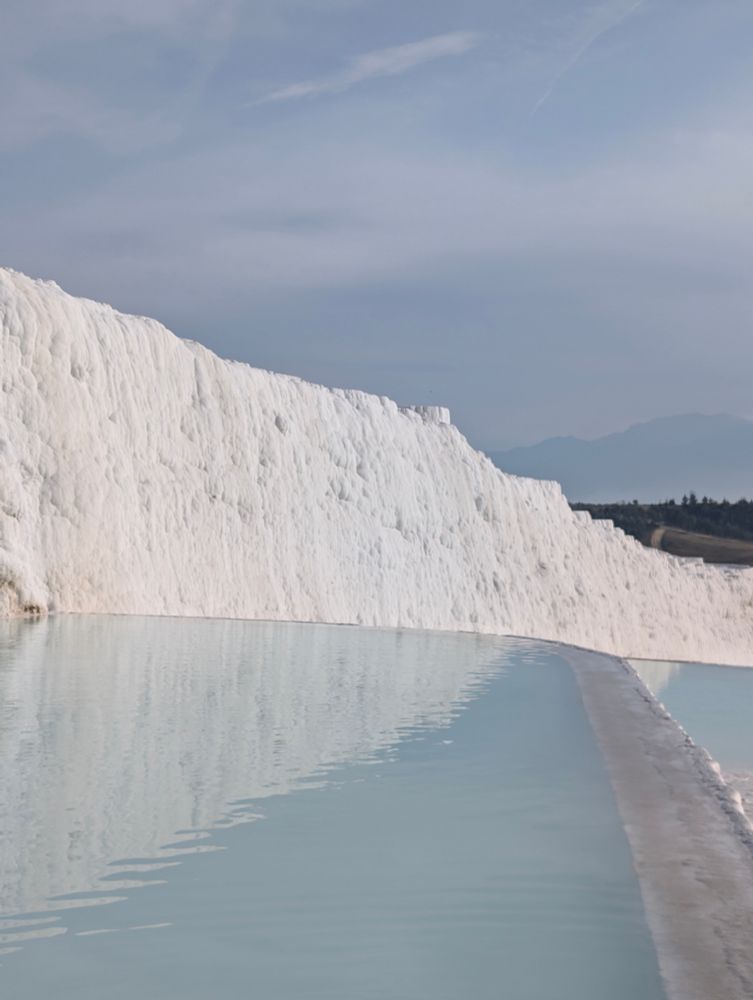 Colour photograph. A turquoise white pool stretches out in front of a white wall of calcium. 