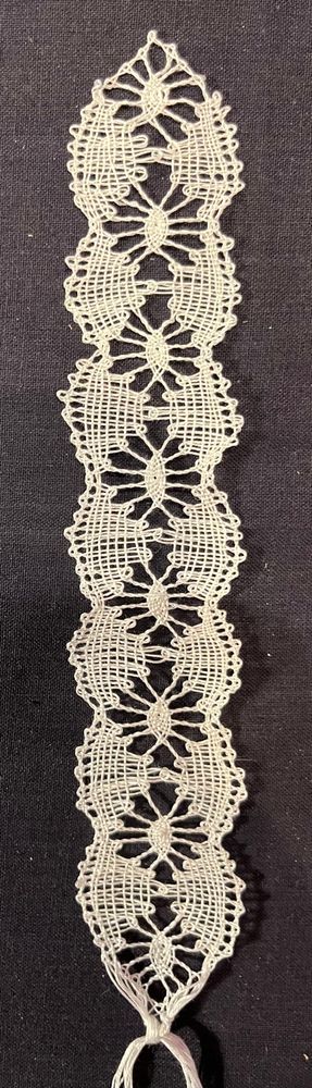 Piece of handmade torchon lace in white. The pattern is a mixture of ‘spiders’ and fans. 
