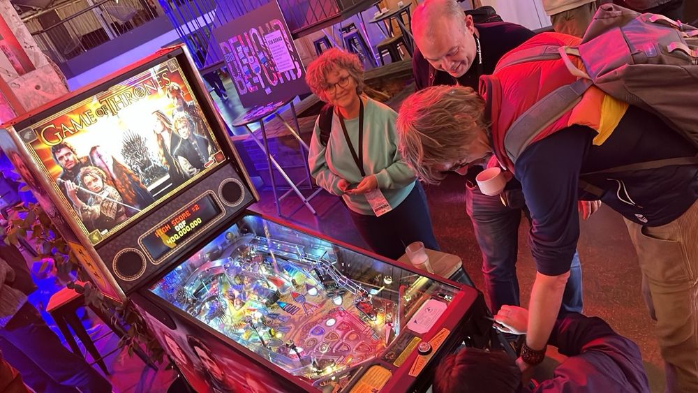 Many people gathering around a Game of Thrones pinball machine at the Beyond Tellerrand lounge