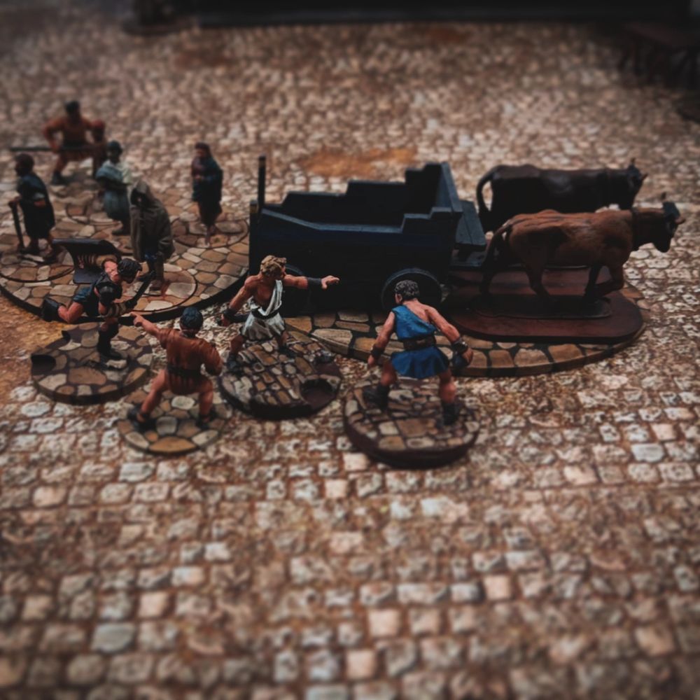 One Roman gang gently encourages an ox cart to move forward, while another tries to stop it. Meanwhile an angry mob of Roman citizens approaches. 
