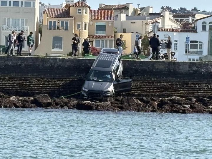 a heavy car fallen from the road and crashed onto rocks, a foot above water