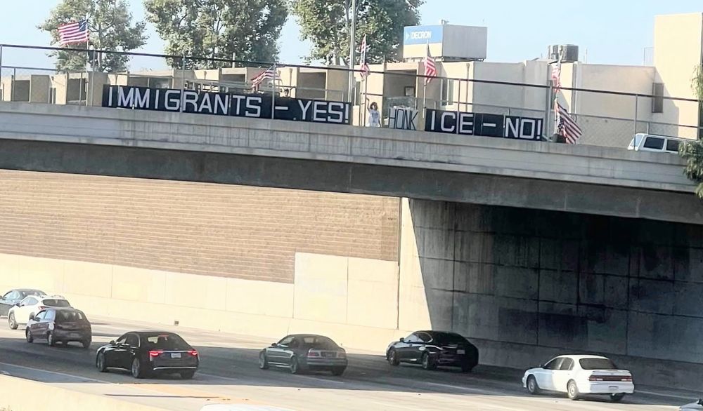 Protesters on overpass waving at drivers below them as they read the message IMMIGRANTS- YES! ICE - NO! 