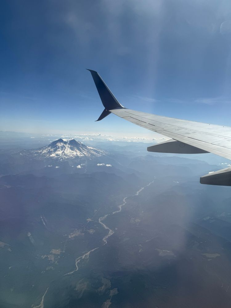 View from an airplane window. Green forests surrounding a snow covered Mount Ranier and a plane wing in the foreground 
