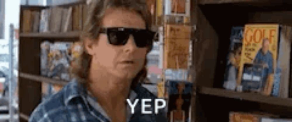 a man wearing sunglasses is standing in front of a book shelf .