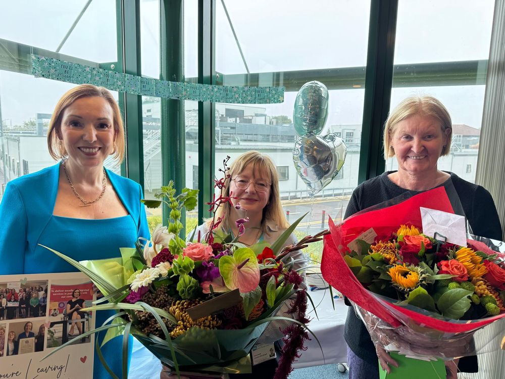  Chief Executive Jennifer Welsh holds a large card, while two others stand beside her holding large bouquets of flowers.