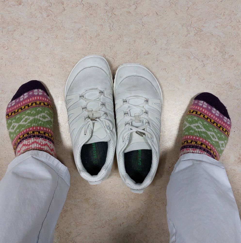 Ein paar Füße in Wollstricksocken nebst einem Paar weißer Barfußschuhe