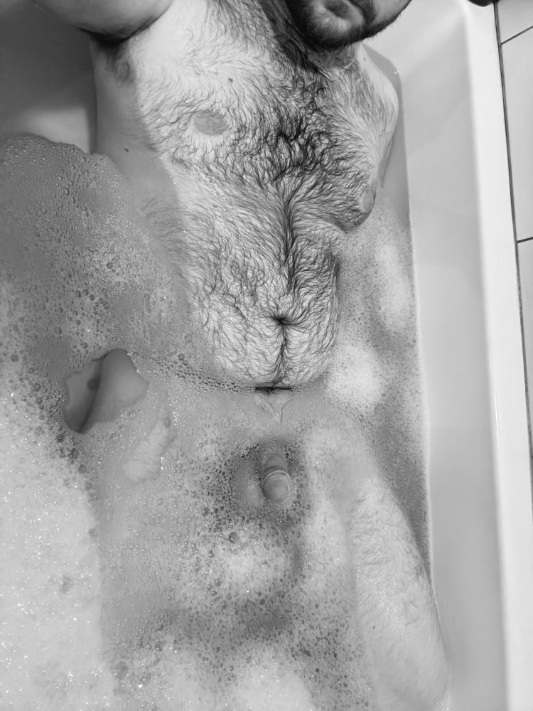 Black and White photo of me laying in the bathtub with my hairy torso and package peeking out through the bubbles.