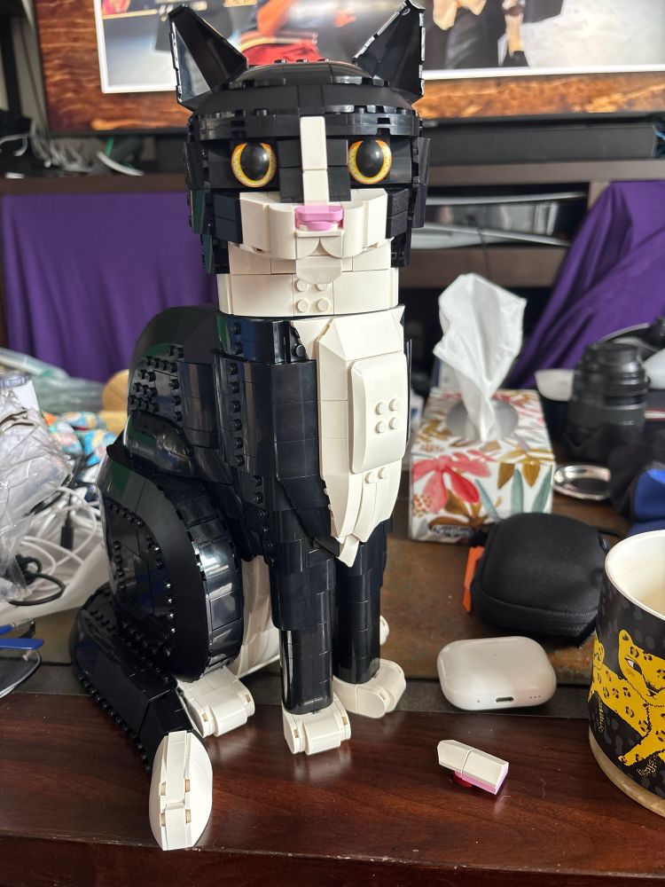A LEGO tuxedo cat sits on a coffee table amidst other random objects.