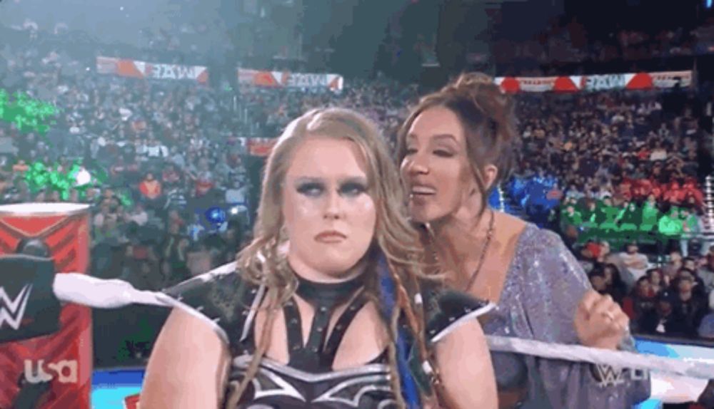 two women are standing next to each other in a wrestling ring with a crowd in the background .