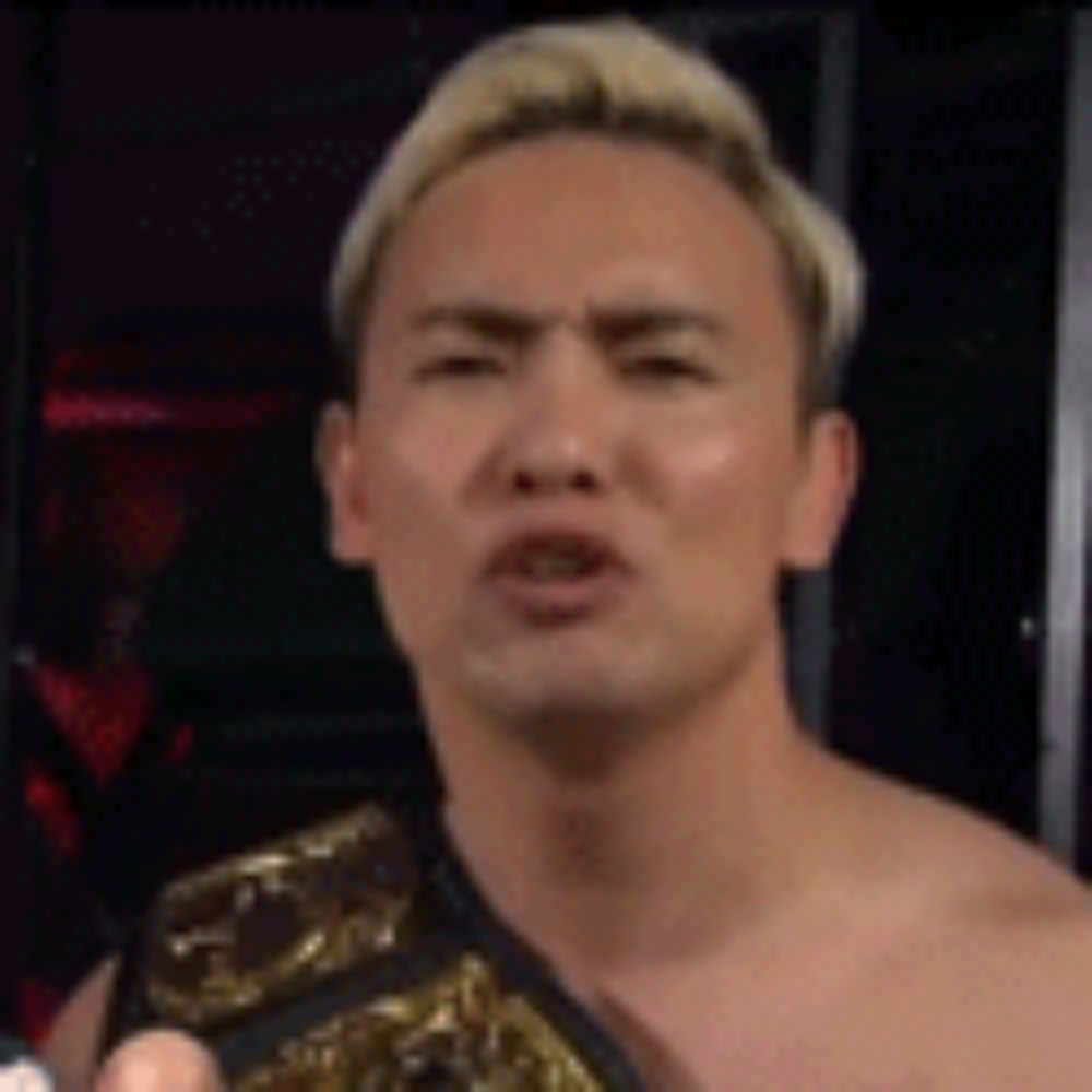 a man without a shirt is wearing a wrestling belt and making a face .