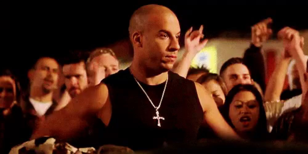 a man wearing a necklace with a cross on it is standing in front of a crowd of people .