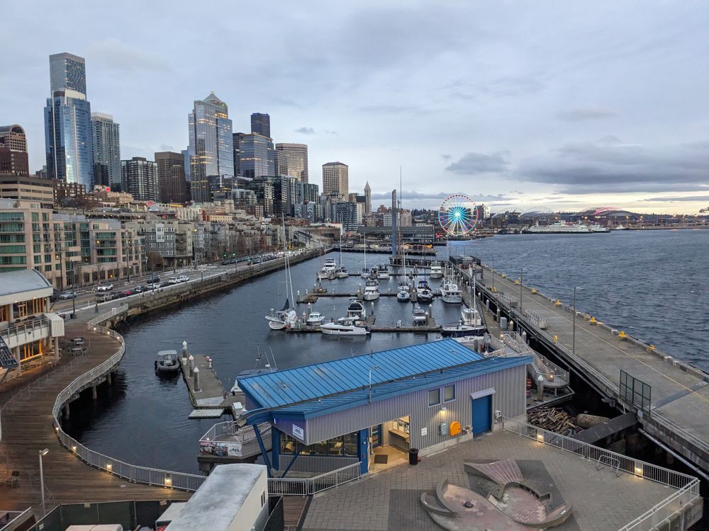 photo over the Seattle waterfront with the bay on the right, docks and boats in the middle, and the city skyline on the left. 