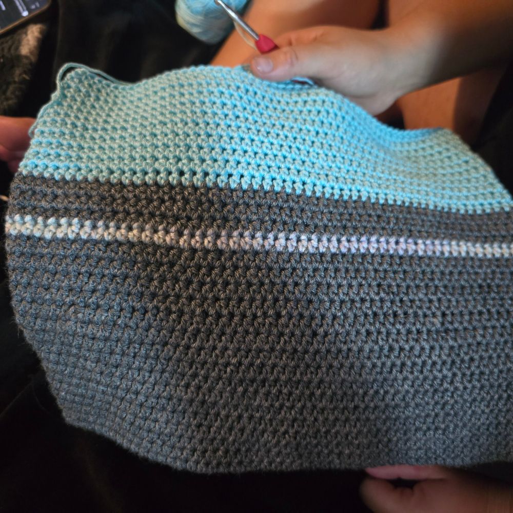 a crocheted tote bag, dark grey on the bottom (so it can be set on dirty surfaces) with a pearlescent stripe and a seamless color change to sky blue