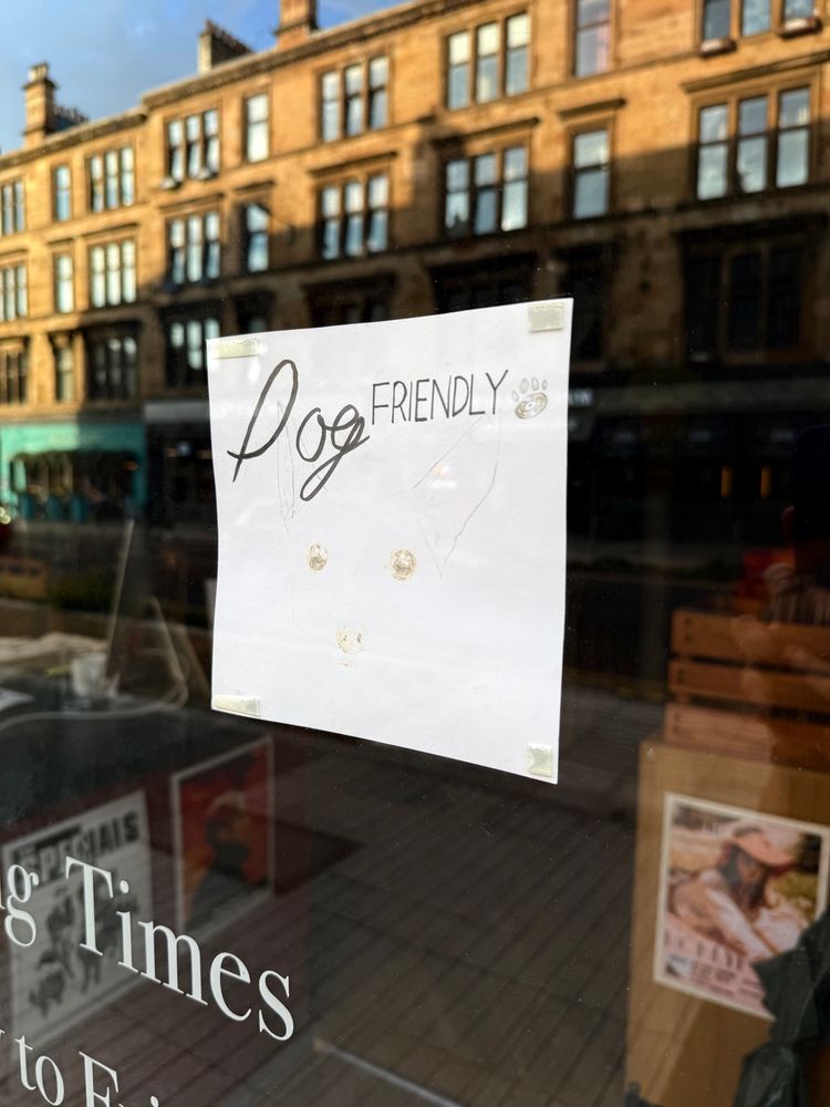 A sign in a shop door says they’re dog friendly. It looks like it used to show a picture of a dog but has almost entirely faded from sunlight exposure, so all you can see is the dog’s eyes and an outline of its nose