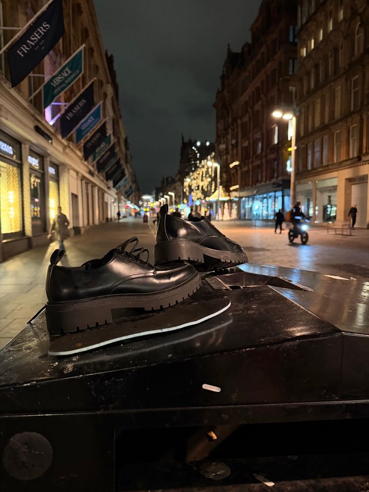 On a moody evening, two matching shiny black shoes in surprisingly good condition have been abandoned on top of a bin on Glasgow’s Buchanan Street