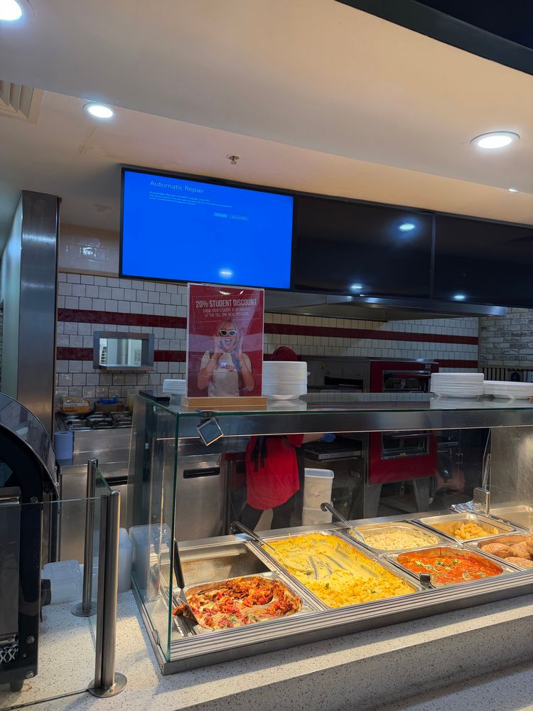 a food counter with pasta dishes on display. there’s large monitors where you would expect a menu to be. the leftmost one has the Windows “Automatic Repair” screen on it, and the others are all blank