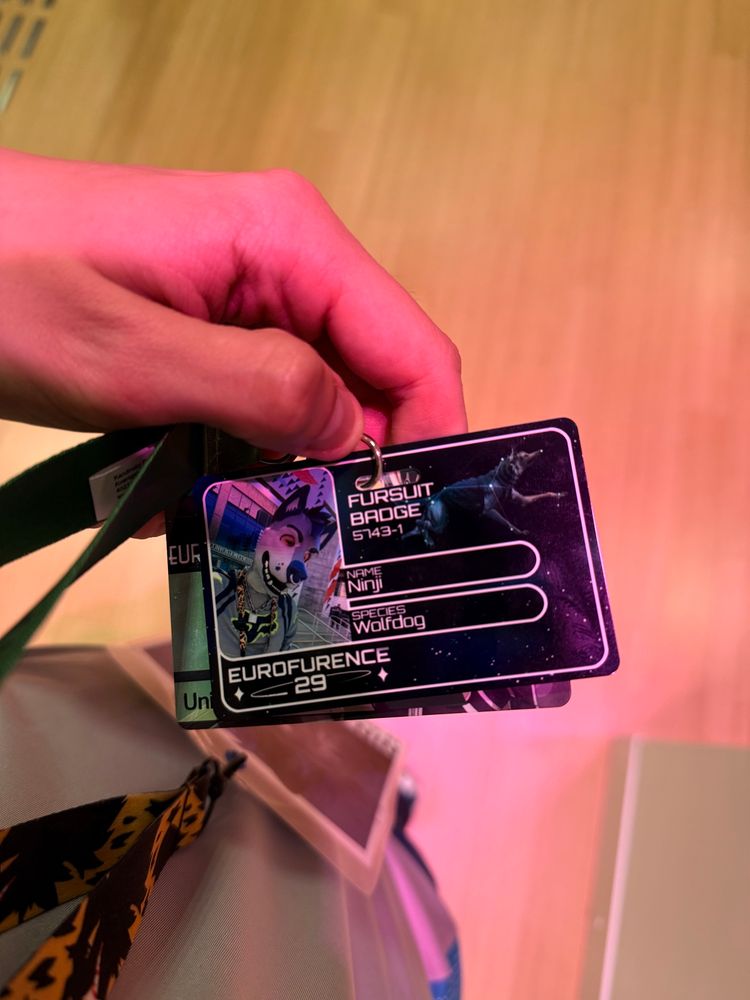 Me holding up my EF fursuit badge, which has a picture of me wearing the shiny dog face and lists my species as Wolfdog