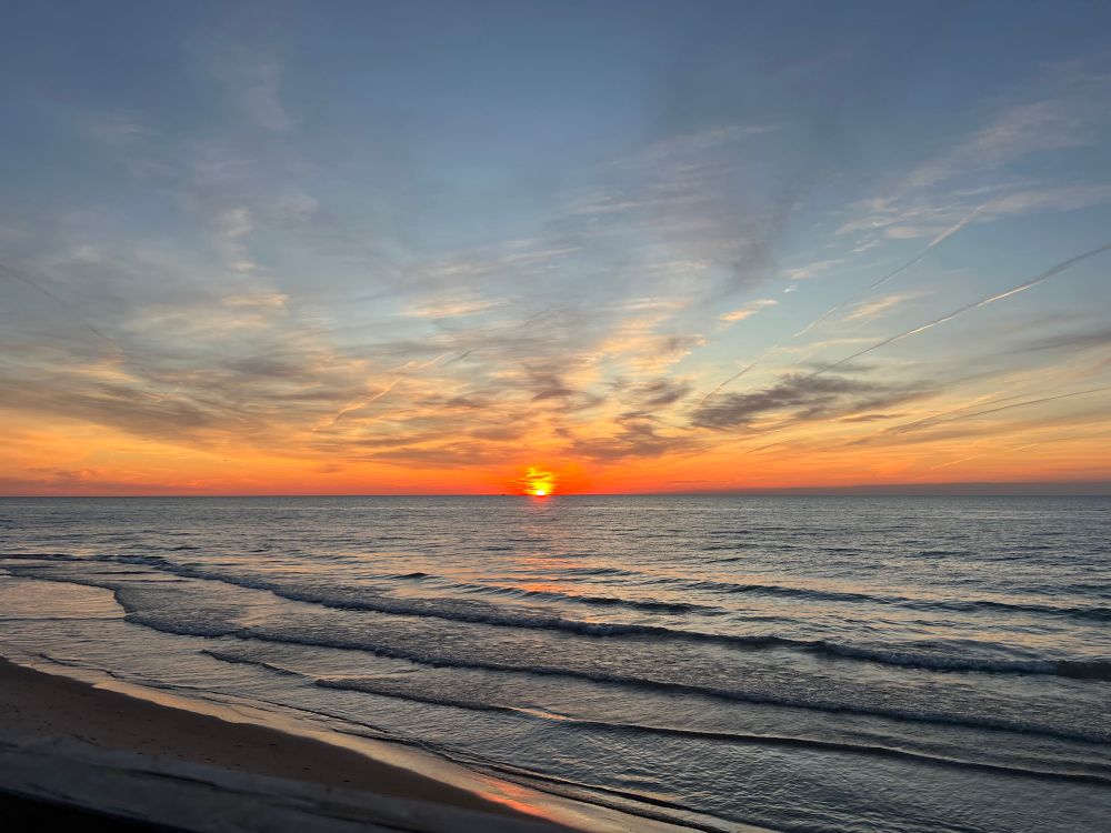 Sunset over Lake Huron with streaks of clouds in the sky and waves crashing upon the beach in the foreground