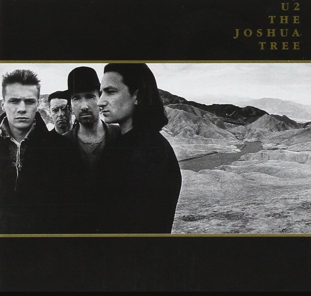 Album cover art for U2: The Joshua Tree featuring a black and white image of the four band members in a desert with rolling hills behind them.
