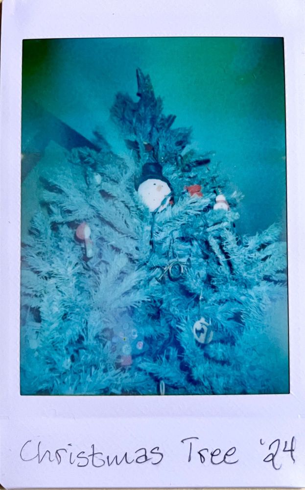 An instant photo of a Christmas tree with a snowman ornament in the center. 