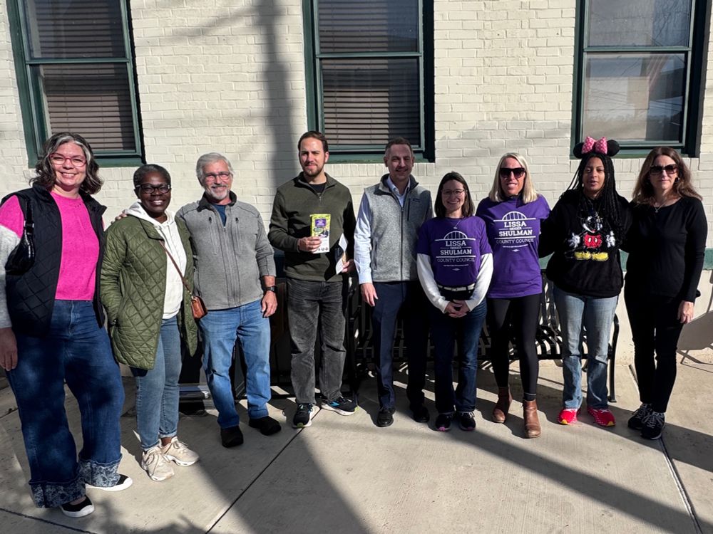 Large group of individuals pictured in front of a brick building with windows. 