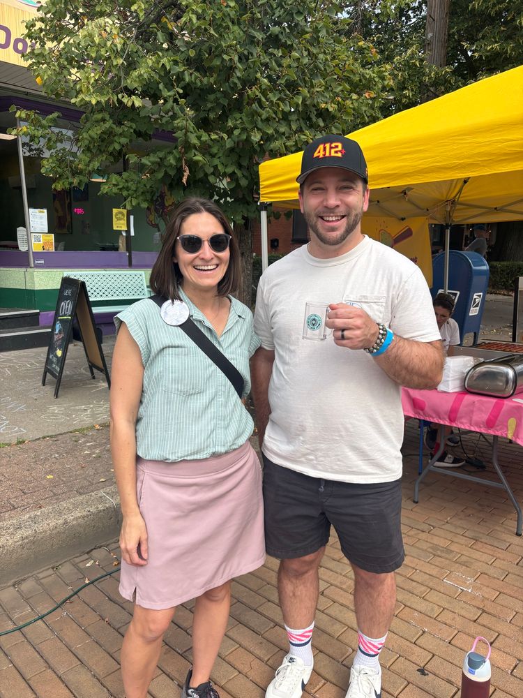 Lissa and an Aspinwall Councilman smiling on a sidewalk on Commercial Ave. with a tent visible behind them.