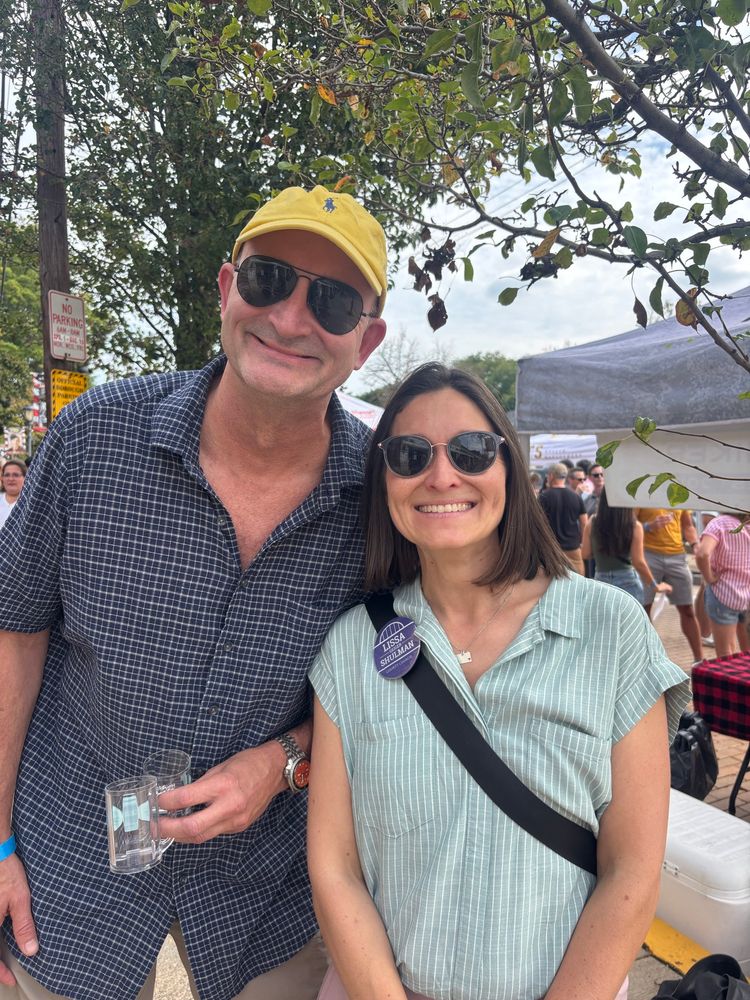 Lissa and an Aspinwall candidate for mayor smiling on a sidewalk on Commercial Ave. with a tent visible behind them.