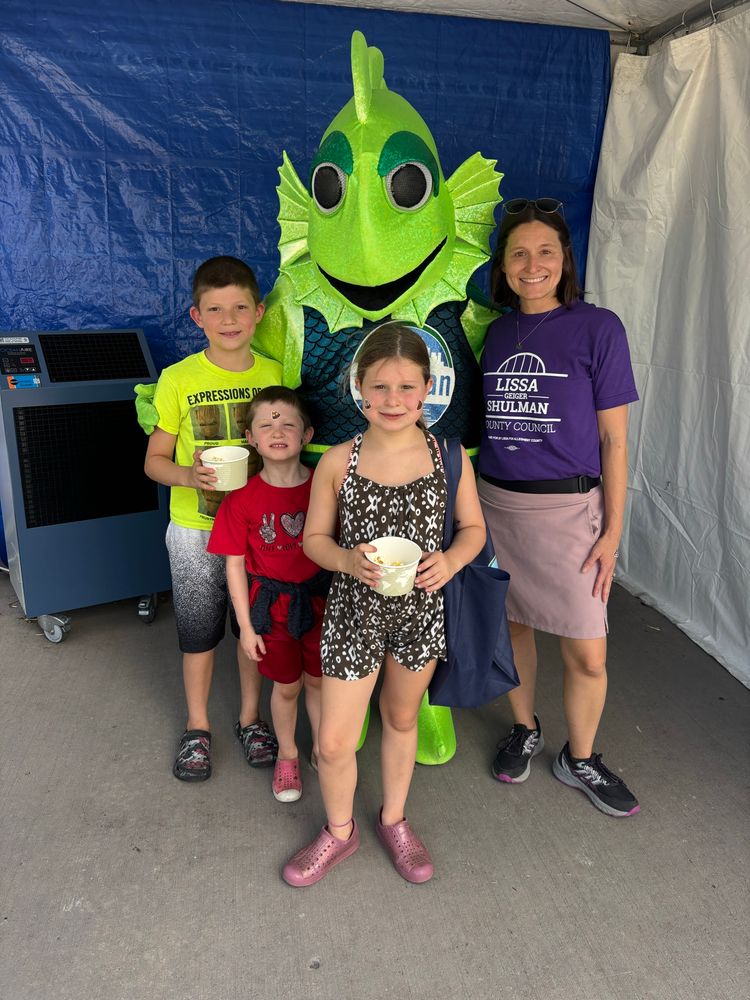 Lissa in a purple campaign T-shirt with her 3 children and Frankie the fish mascot standing behind them. All looking at camera and smiling.