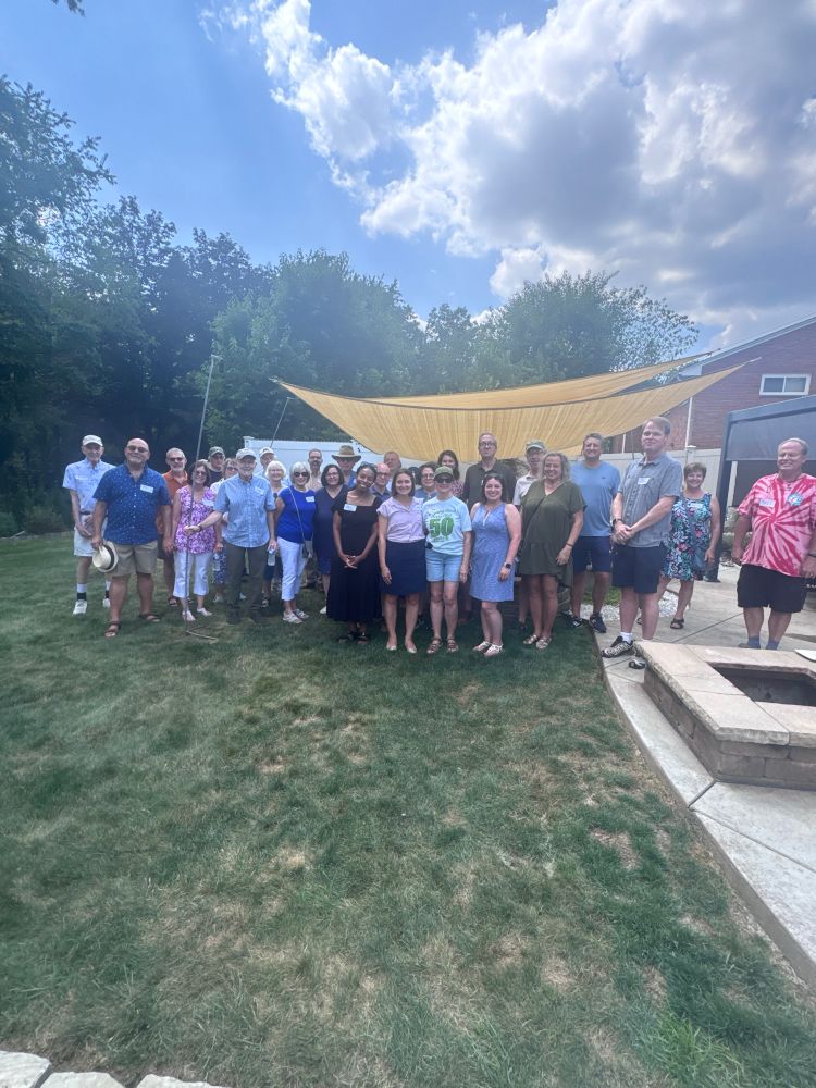 Large group of supporters standing with Lissa, Rep. Powell, and Sen Williams and a woman in a sierra club tshirt at the front. A blue sky with clouds, green grass, and patio are visible behind the group.