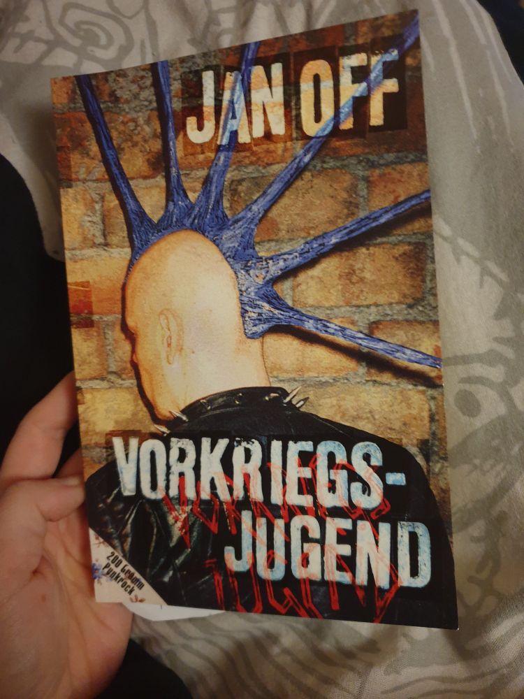 Buch-Cover: männlicher Punk mit blau gefärbten Stachel-Iro-Haaren steht schräg mit dem Gesicht zu einer Wand. Auf dem Rücken steht der Buchtitel "Vorkriegs-Jugend" und oben auf dem Cover der Autor "Jan Off".