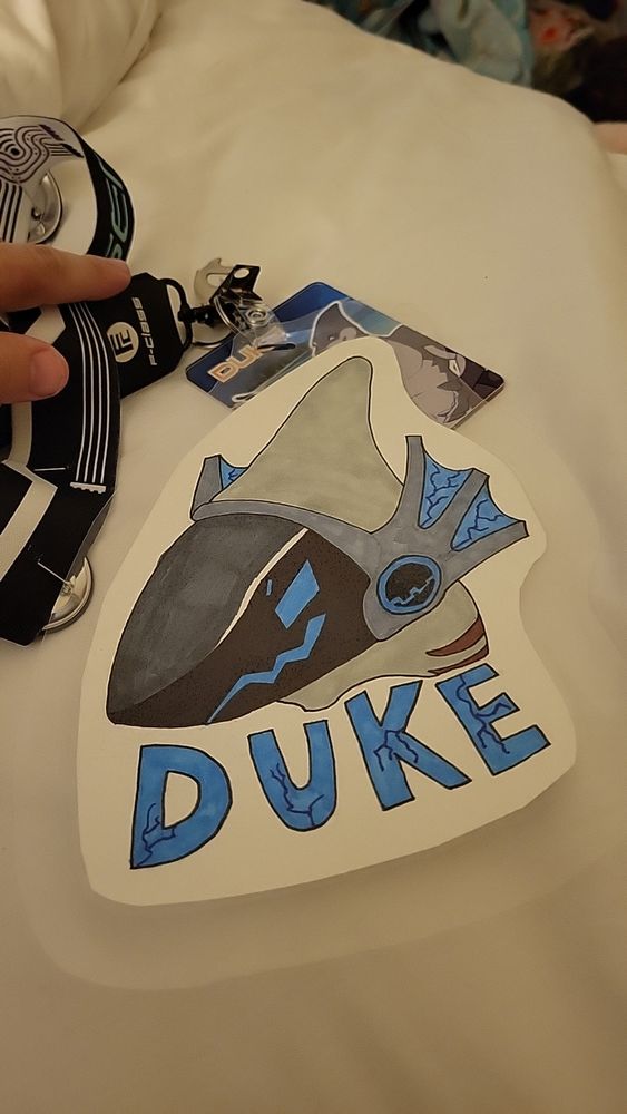 A picture of a robot shark head with blue lights for eyes and a mouth on a black tinted visor for a head. A sign below it that spells DUKE