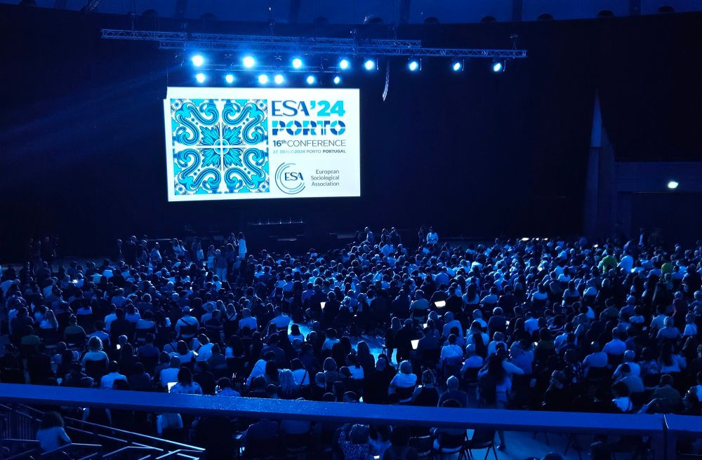 Inside the Bock Arena before the opening ceremony for the ESA. Hundreds of sociologists sit in the air-conditioned and darkened hall. Title slide of the conference presentation at the front above the stage.