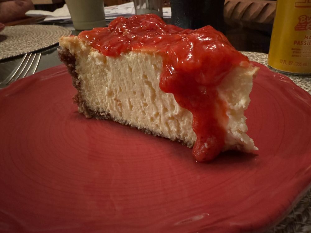 Slice of leftover cheesecake with homemade strawberry topping on top of a red plate. 
