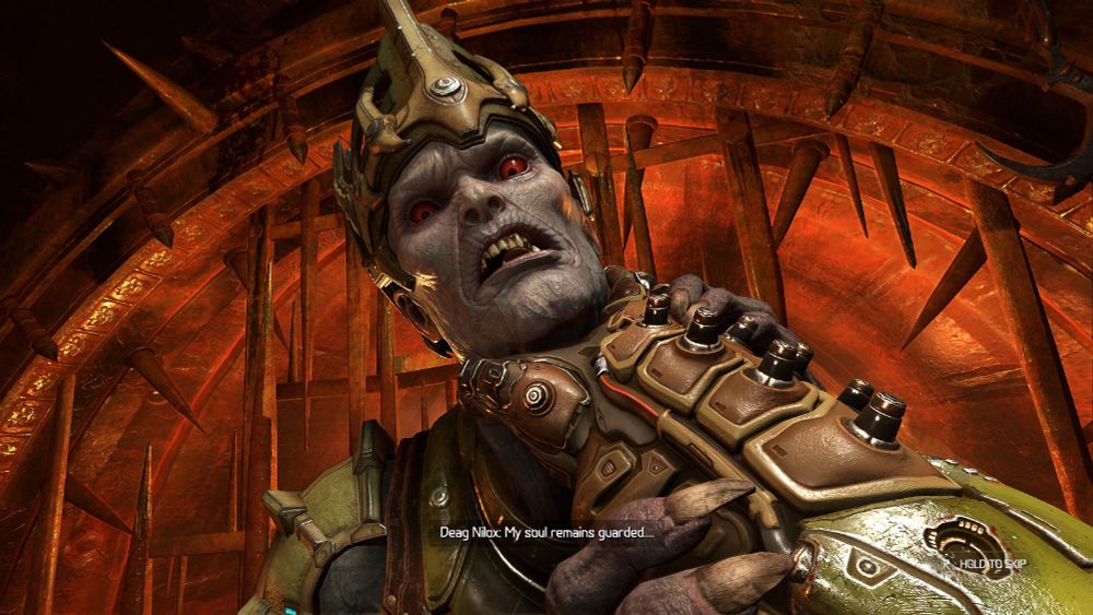 A Doom Eternal screenshot. First-person view of Doom Guy's armoured hand grabbing the neck of a withered hold Hell Priest, who has grey skin and red eyes and manky teeth. They're in trouble.