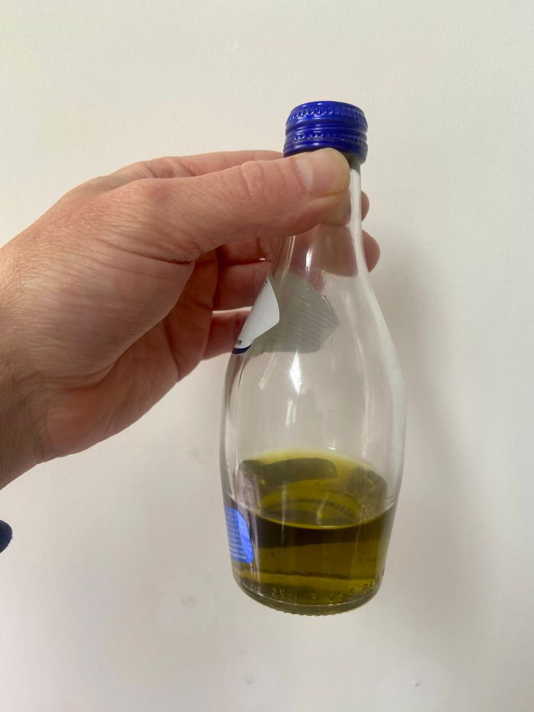 A hand holds a bottle with some olive oil in it