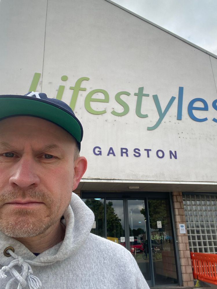 A man with a blue cap and grey hoodie standing in front of the swimming baths