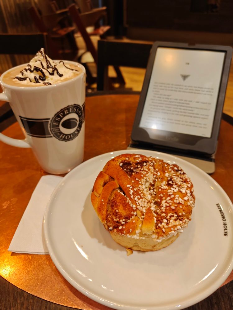 A kanelsnegl with a mocha latte and an ereader all upon a round table in a cafe 