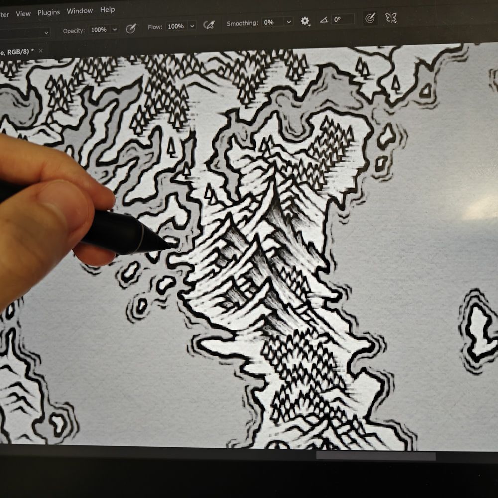 A hand grasping a pen that hovers above a display tablet which has a work in progress black and white fantasy map on it. Some of the mountains are shaded while others still await the gentle strokes of the pen to provide them with shade.