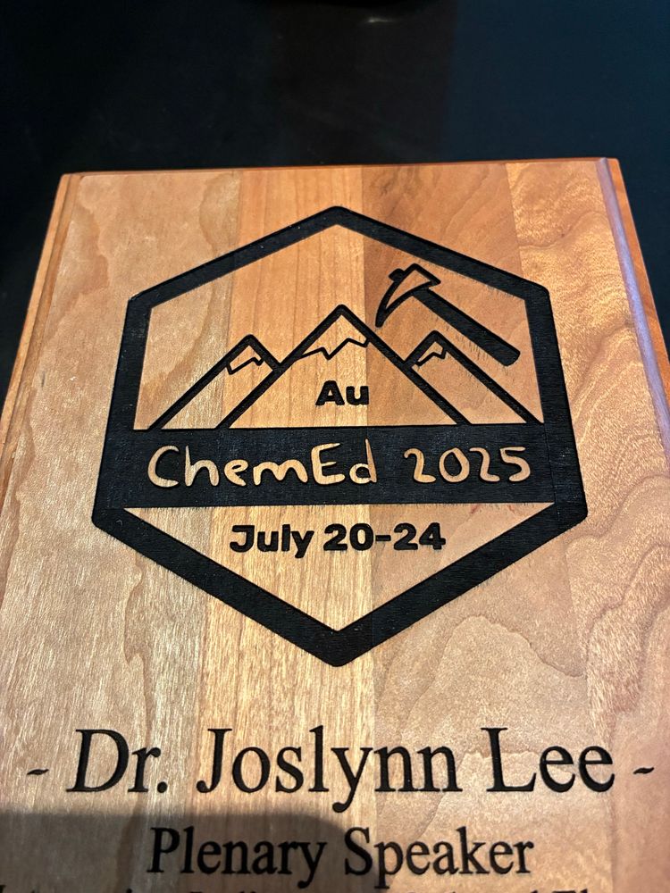 Wooden plaque with mountain etched with element symbol Au above text reading Chem Ed 2025 July 20-25 and below the image Dr. Joslynn Lee plenary speaker. 