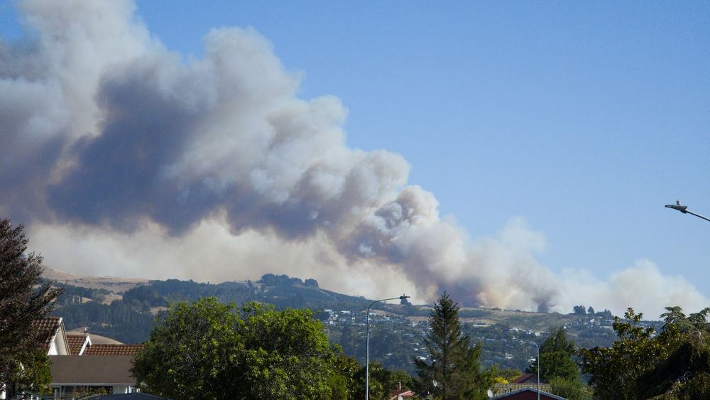 Thick billowing grey and yellowish smoke rising from a fire in the Port Hills of Christchurch