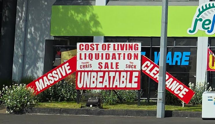 A sign advertising a "Cost of Living Liquidation Sale" with additional wording "Thanks Chris" and "You Suck" which I can only assume is aimed at our worse-than-useless Prime Minister Christopher Luxon.