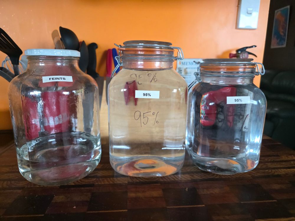 A jar with some feints (undrinkable alcohol that will be re distilled next time) and two big jars of neutral spirits waiting to be diluted down to drinkable strength. 