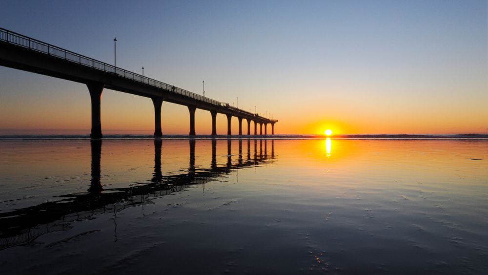 The rising sun peeps over the ocean behind New Brighton pier, Christchurch NZ