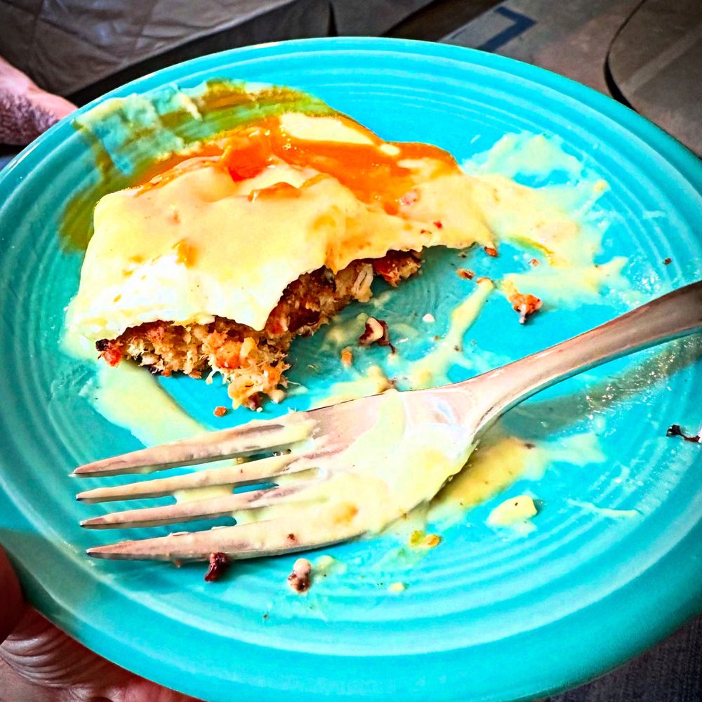 A teal plate with crab cakes eggs Benedict, half eaten. 