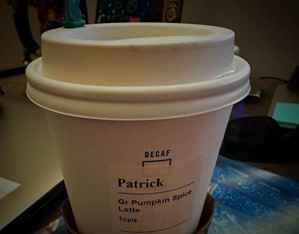 A grande Starbucks Pumpkin Spice Latte for Patrick, sitting on an anime mouse pad, with a splash stopper inserted. 