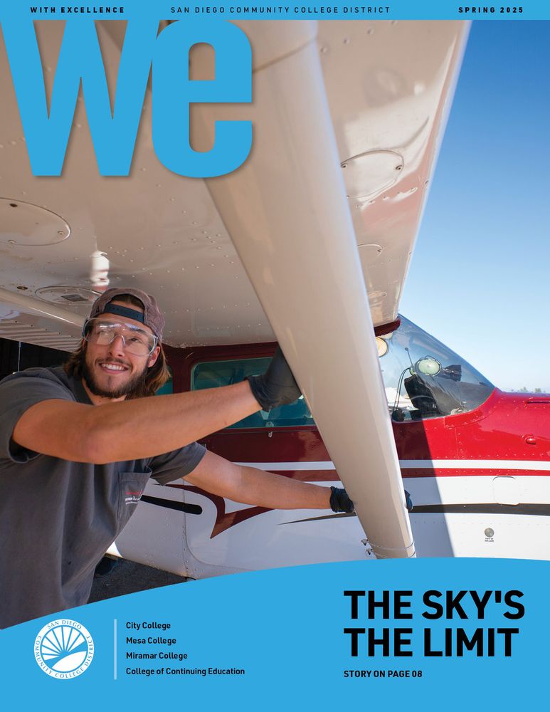 An aviation student wearing protective goggles and gloves pushes a small red and white plane on a runway
