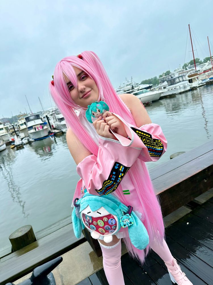 Sakura Miku cosplayer holding small miku plushie
